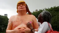 Seorang nenek memegang kepala patung Donald Trump tanpa busana yang dipajang di Union Square Park, AS, Kamis (18/8). Warga di sekitar Union Square Park, New York, rela mengantre untuk berfoto dengan patung tersebut. (REUTERS/Brendan McDermid)
