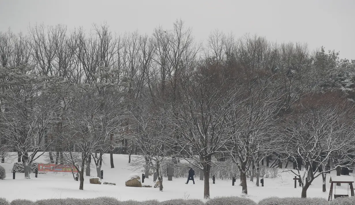 Pengunjung berjalan di salju dekat spanduk instruksi jarak sosial sebagai tindakan pencegahan virus corona di sebuah taman di Goyang, Korea Selatan, Kamis (28/1/2021). Hujan salju diperkirakan akan turun di sebagian besar negara itu pada hari Kamis dengan angin kencang kelas topan. (AP/Lee Jin-man)