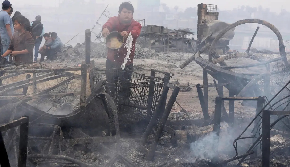 Seorang pria menyiram bara api yang masih tersisa akibat kebakaran yang melanda permukiman Cantagallo di Lima, Peru, Jumat (4/11). Petugas masih menyelidiki penyebab kebakaran di permukiman yang dihuni komunitas Suku Amazon itu. (REUTERS/Guadalupe Pardo)
