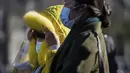Seorang wanita yang mengenakan masker untuk membantu mengekang penyebaran virus corona mengenakan tudung bulunya saat berjalan di distrik perbelanjaan Wangfujing saat ibu kota dilanda angin dingin di Beijing, Minggu (12/12/2021).  (AP Photo/Andy Wong)