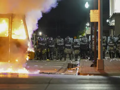 Polisi berdiri dekat truk sampah yang terbakar saat protes di Kenosha, Wisconsin, Amerika Serikat, Senin (24/8/2020). Protes dipicu oleh penembakan Jacob Blake oleh petugas polisi Kenosha sehari sebelumnya. (AP Photo/Morry Gash)