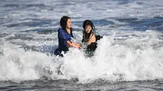Dua wanita menikmati ombak di sepanjang pantai dekat Pulau Enoshima di pantai Prefektur Kanagawa, barat daya Tokyo (13/8/2019). Enoshima adalah pulau lepas pantai kecil, sekitar 4 km di sekelilingnya, di mulut Sungai Katase yang mengalir ke Teluk Sagami di Prefektur Kanagawa, Jepang. (AFP Photo/Char