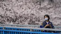 Seorang wanita mengenakan pakaian tradisional Kimono melihat kanopi bunga sakura saat dia melewati jembatan penyeberangan di Tokyo, Jepang, Minggu (27/3/2022). (AP Photo/Kiichiro Sato)