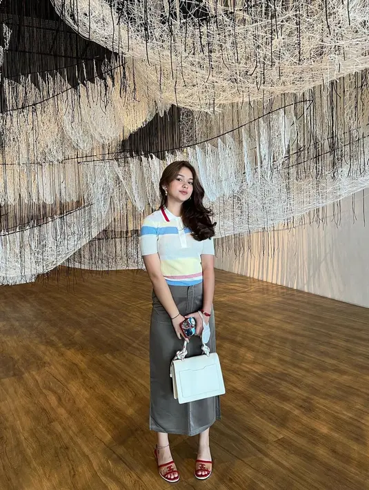 Inspirasi outfit untuk museum date dari Rebecca Klopper. Ia mengenakan atasan lengan pendek bergaris bernuansa biru, dipadu dengan rok cokelat, sandal slip on, dan tas. Foto: Instagram.