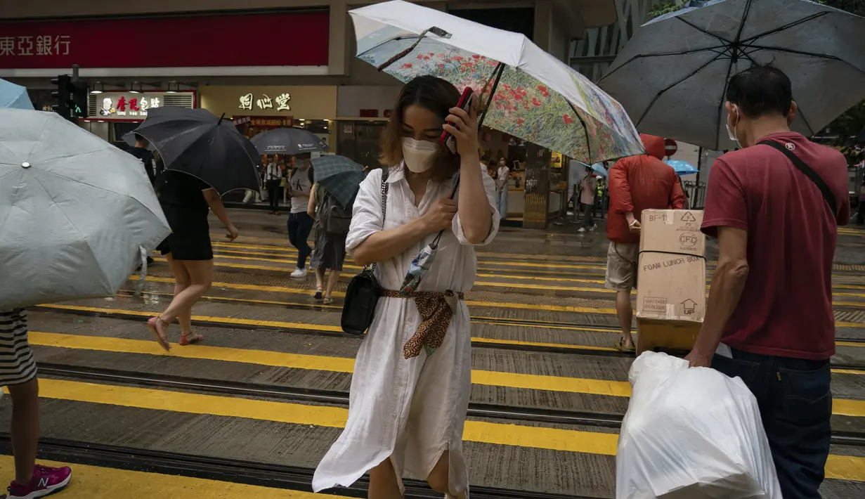 Orang-orang memegang payung di bawah angin kencang berjalan melewati penyeberangan saat badai tropis Ma-on melewati Hong Kong, Kamis (25/8/2022). Badai Tropis Ma-on semakin kuat saat menuju Hong Kong dan bagian tenggara lainnya China pada hari Rabu setelah menggusur ribuan orang di Filipina. (AP Photo/Anthony Kwan)