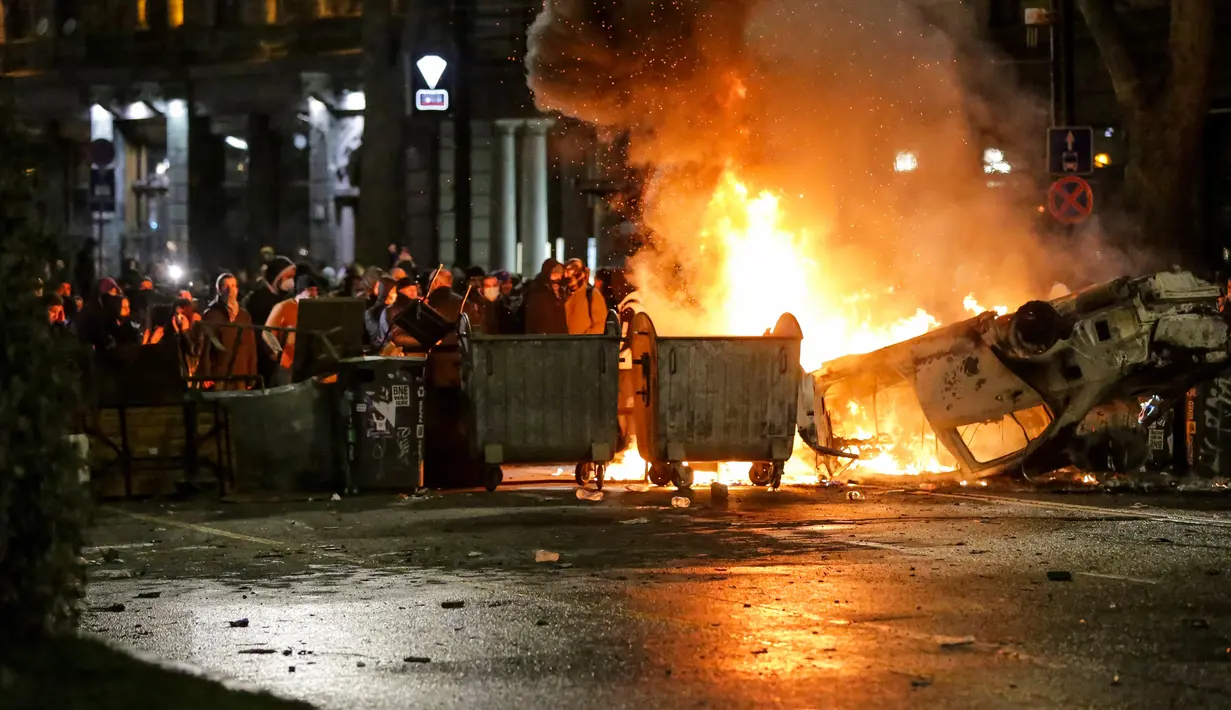 Para pengunjuk rasa berkumpul pada barikade dengan mobil polisi yang terbakar tidak jauh dari Gedung Parlemen Georgia di Tbilisi, Georgia, Kamis (9/3/2023). Tahun lalu, Georgia adalah salah satu negara yang ditolak Uni Eropa untuk mendapatkan status negara calon anggota, selain Moldova dan Ukraina, dengan alasan ketiga negara itu lamban mereformasi politik dan sistem peradilan mereka. (AP Photo/Zurab Tsertsvadze)