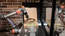 Robot pembuat pizza Bernama "Pazzi" sedang bekerja di sebuah restoran di Paris pada 1 Juli 2021. Pazzi menyiapkan, mengiris bahan, memanggang, dan mengepak piza hingga akhirnya sampai ke tangan pelanggan. (BERTRAND GUAY/AFP)