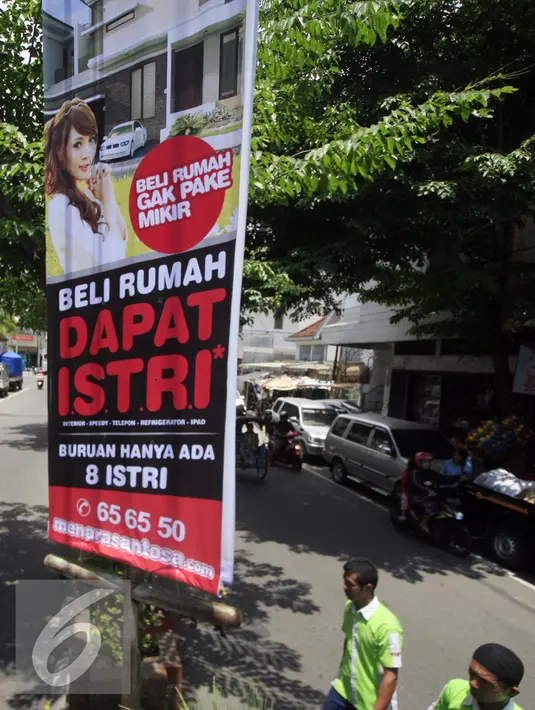 Dua Karyawan toko melintasi benner ilklan beli rumah dapat istri di kawasan Nonongan, Solo (3/2/2016). Iklan di pasang untuk menarik minat calon pembeli. (Liputan6.com/Boy Harjanto)