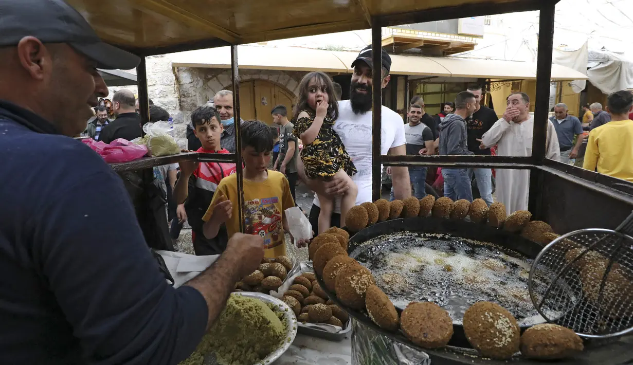 Seorang gadis Palestina makan sepotong falafel di sebuah pedagang di kota Hebron di Tepi Barat yang diduduki, selama bulan suci Ramadhan, Minggu (18/4/2021). Falafel adalah sebuah makanan Timur Tengah yang pada bulan Ramadhan, sering dimakan sebagai hidangan buka puasa. (HAZEM BADER/AFP)