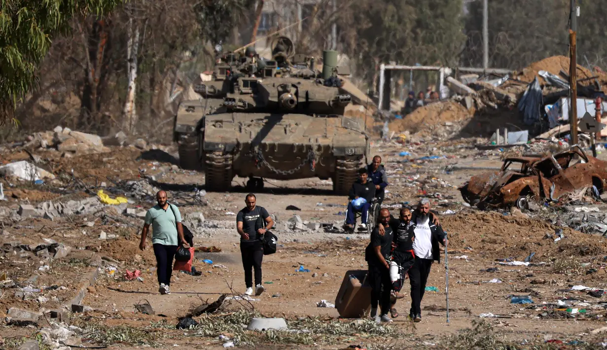 Warga Palestina yang melarikan diri dari utara melalui jalan Salaheddine di distrik Zeitoun di pinggiran selatan Kota Gaza berjalan melewati tank-tank tentara Israel pada 24 November 2023 setelah gencatan senjata selama empat hari yang dimulai sejak pagi hari. (MAHMUD HAMS/AFP)