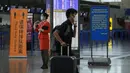 Seorang penumpang mendorong barang bawaannya melewati staf pesawat yang berdiri di dekat konter check-in yang sepi di Bandara Internasional Pudong, Shanghai, Minggu (25/7/2021). Ratusan jadwal penerbangan dibatalkan saat topan In-Fa bergerak menuju mendarat. (AP Photo/Andy Wong)