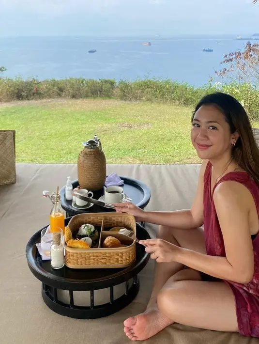 Sherina tampil simple dengan dress merah sambil makan dengan pemandangan samudra. Bagian wajah, Sherina memilih makeup flawless