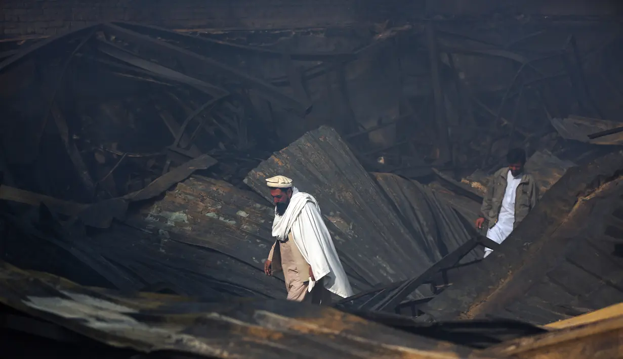 Dua pria berjalan di antara reruntuhan setelah kebakaran menghanguskan pasar peralatan elektronik di Kabul, Afghanistan (2/11). Warga ibukota Afghanistan bergulat memadamkan kobaran api besar yang menghancurkan ratusan toko. (AP Photo/Massoud Hossaini)