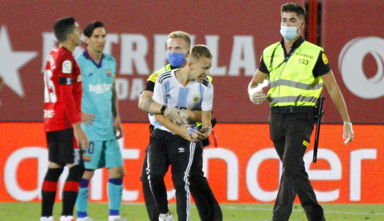 Petugas keamanan menangkap seorang fans yang nekat menerobos lapangan saat pertandingan antara Mallorca melawan Barcelona di Stadion Son Moix, Minggu (14/6/2020). Fans tersebut ingin berfoto dengan Lionel Messi. (AP/Francisco Ubilla)