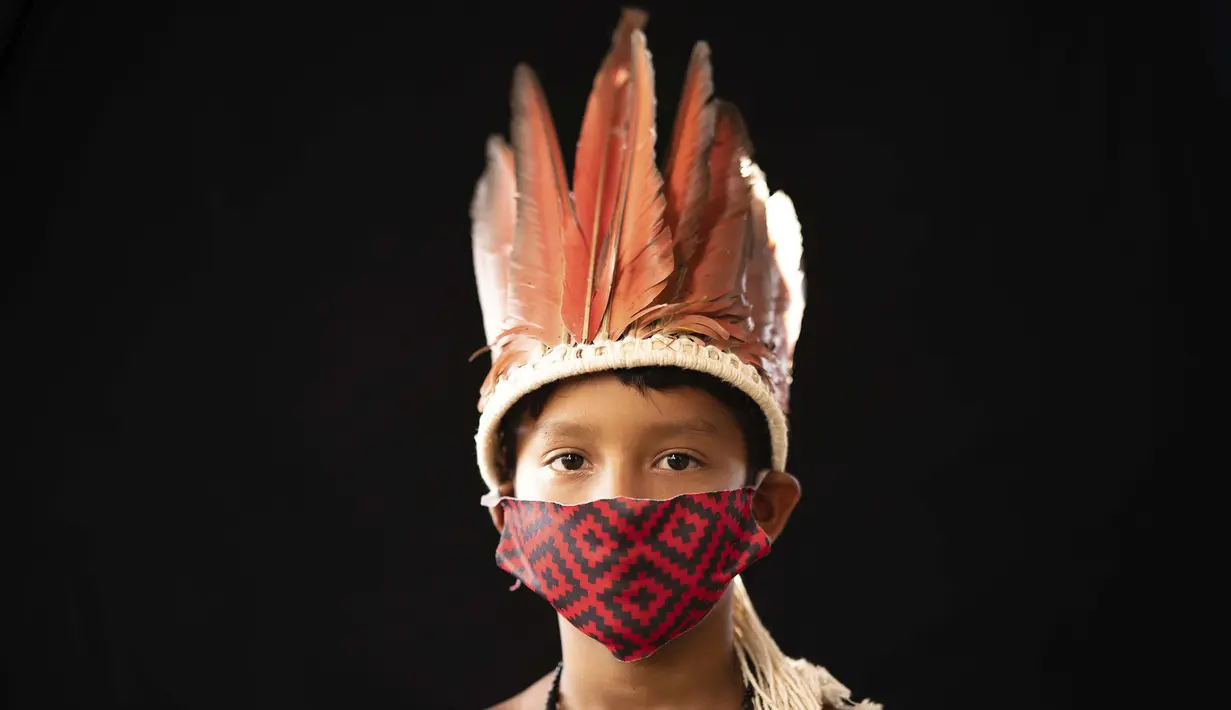 Elano de Souza (6) dari kelompok etnis pribumi Sateré Mawé mengenakan pakaian tradisional sukunya dan masker saat pandemi virus corona COVID-19 di daerah Gaviao, dekat Manaus, Brasil, Jumat (29/5/2020). (AP Photo/Felipe Dana)