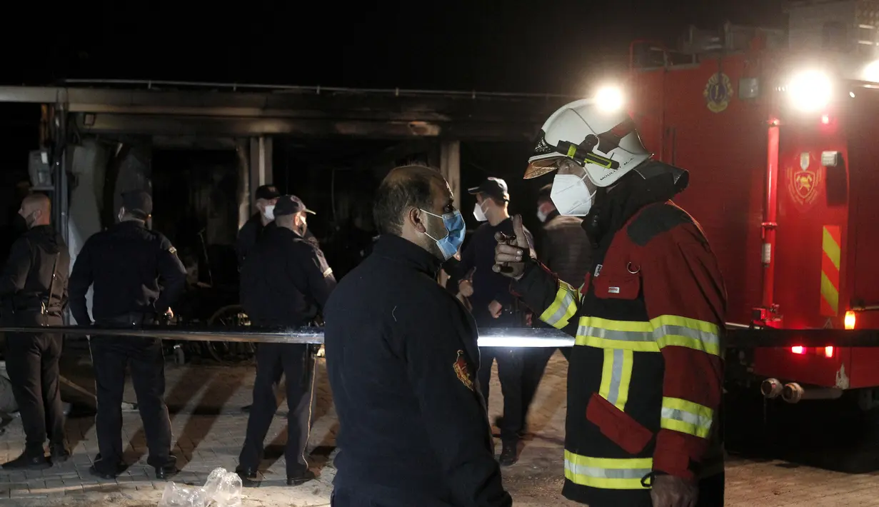 Petugas pemadam kebakaran berbicara satu sama lain berdiri di dekat rumah sakit darurat yang terbakar di kota Tetovo, Makedonia Utara, Kamis (9/9/2021). Kebakaran terjadi Rabu malam di rumah sakit darurat untuk pasien COVID-19. (AP Photo/Boris Grdanoski)