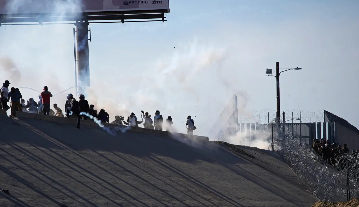 Imigran menghindari gas air mata petugas patroli perbatasan AS di dekat pagar pembatas antara Meksiko dan Amerika Serikat di Tijuana, Meksiko (25/11). Walikota Tijuana telah menyatakan krisis kemanusiaan di kota perbatasannya. (AP Photo/Ramon Espinosa)