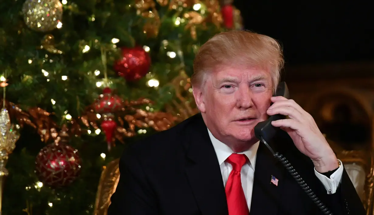 Ekspresi Presiden AS Donald Trump saat berbicara dengan anak-anak di telepon di Palm Beach, AS (24/12). Pada malam natal ini Trump dan istrinya sibuk mendengarkan permintaan anak-anak kepada Sinterklas. (AFP Photo/Nicholas Kamm)