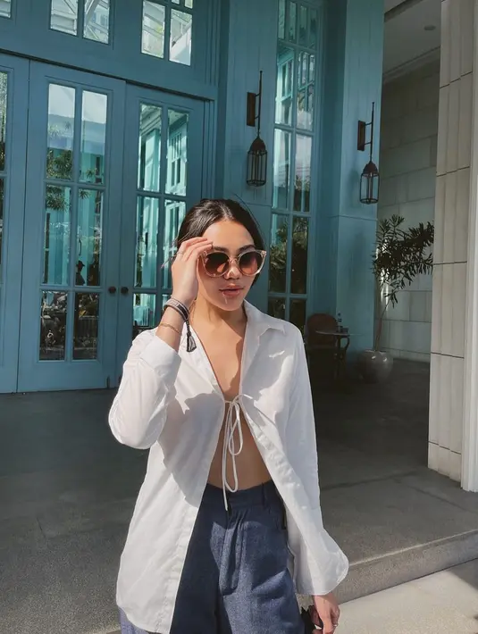 Potret penampilan berani Aaliyah Massaid. Di sini ia mengenakan kemeja putih lengan panjang dengan tali di bagian atas yang memperlihatkan area tubuhnya di bagian depan, dipadu dengan celana biru. [Foto: Instagram/aaliyah.massaid]