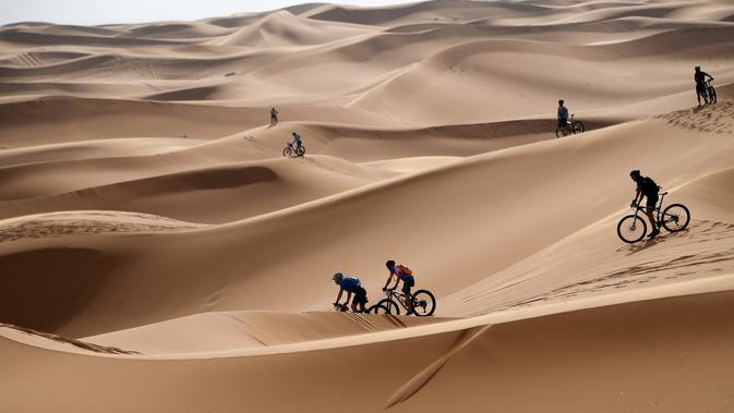 Para pebalap mengendarai sepeda melintasi sepanjang bukit pasir pada etape 1 edisi ke 14 balap sepeda gunung Titan Gurun 2019 di sekitar Kota Merzouga, Maroko, Minggu (28/4/2019). Trek Titan Gurun 2019 sepanjang 640 km menghubungkan antara Merzouga dan Maadid. (Franck Fife / AFP)