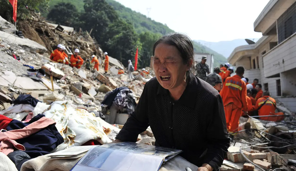 Seorang wanita menangis sambil memegangi album di atas puing-puing rumahnya yang hancur akibat gempa di Longtoushan, provinsi Yunan, Tiongkok, (6/8/2014). (REUTERS/Stringer)