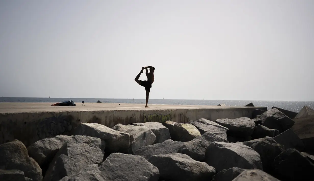 Seorang pria berlatih yoga di tepi pantai di Barcelona, Spanyol, Kamis (12/8/2021). Layanan cuaca nasional Spanyol memperingatkan suhu bisa mencapai 44 derajat Celcius (111 derajat Fahrenheit) di beberapa daerah dalam beberapa hari mendatang. (AP Photo/Joan Mateu Parra)