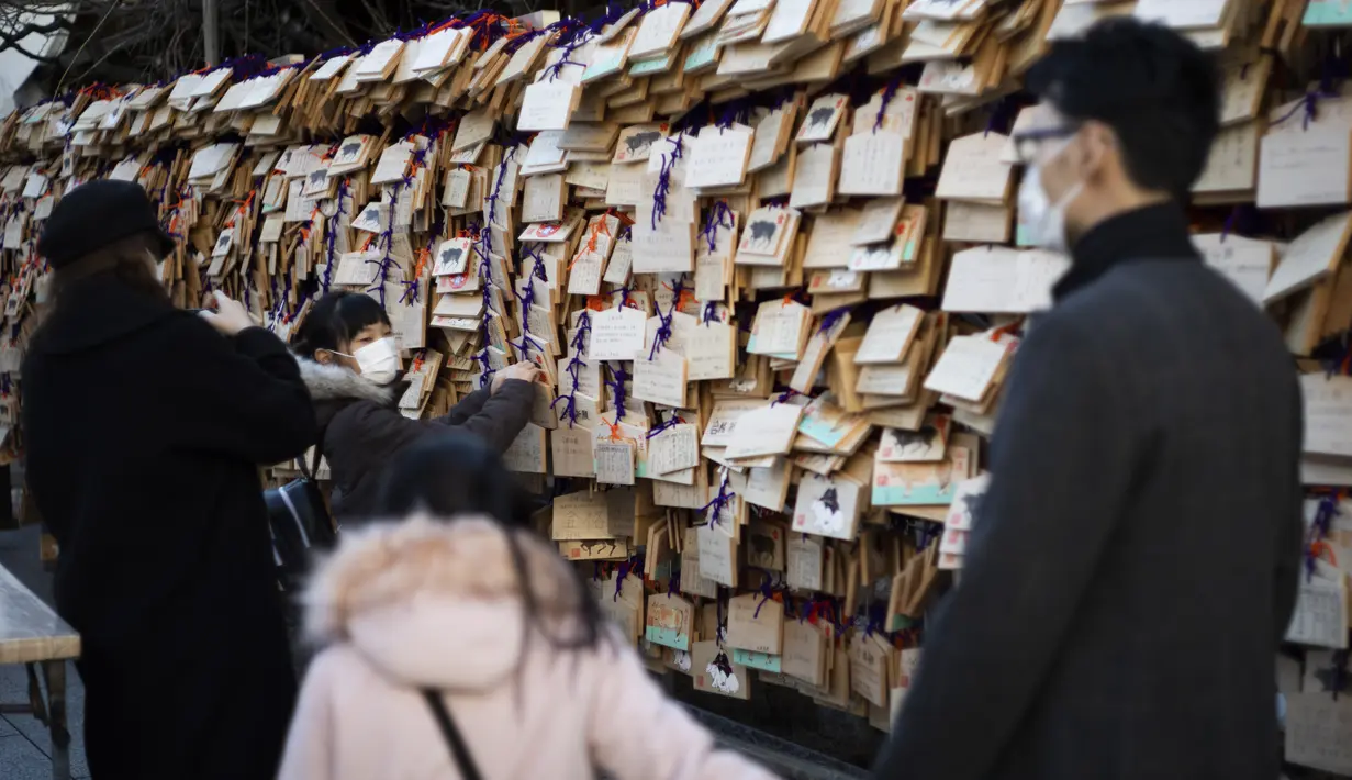 Seorang gadis menggantung papan "ema" dengan keinginannya tertulis di atasnya di kuil Yushima Tenmangu di Tokyo pada Hari Tahun Baru, Jumat (1/1/2021). Papan tersebut biasanya ditulisi dengan doa atau harapan penulisnya agar lebih cepat dikabulkan oleh dewa.  (AP Photo/Hiro Komae)