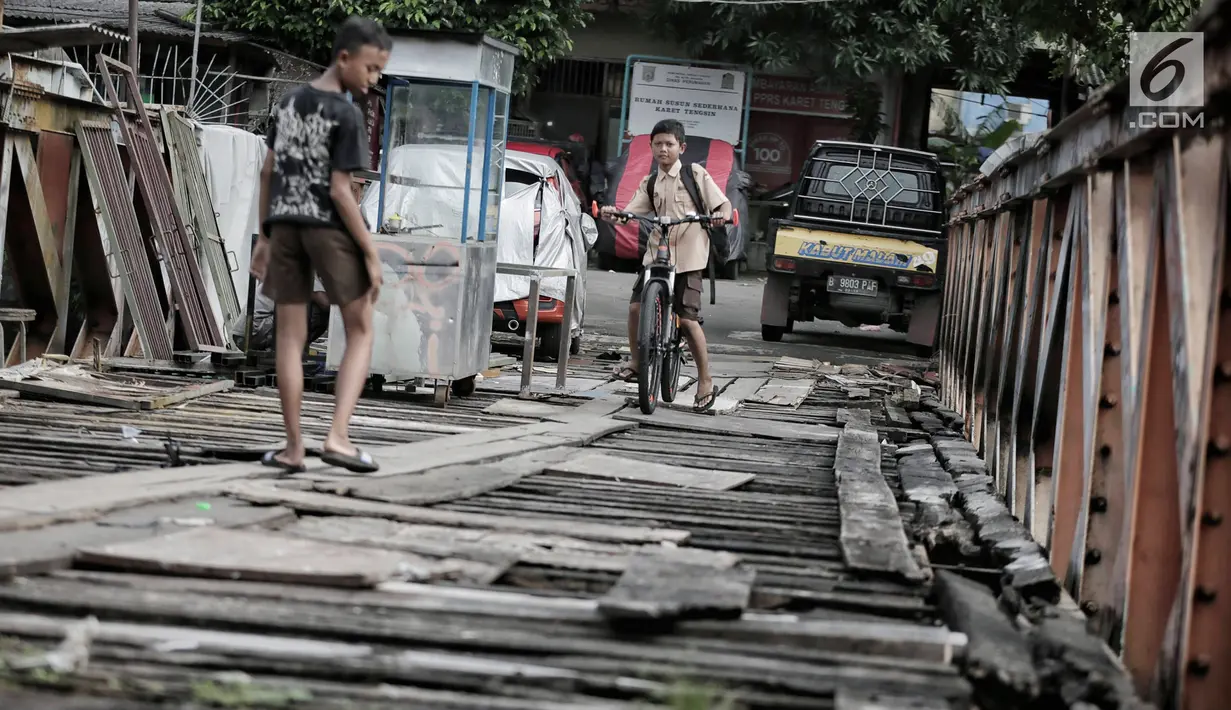 Anak anak melintasi jembatan dari kayu yang menjadi penghubung antara Jalan Karet Pasar Baru VII, Karet Tengsin dan Jalan Pam Baru, Bendungan Hilir, Tanah Abang, Rabu (30/1). (Liputan6.com/Faizal Fanani)