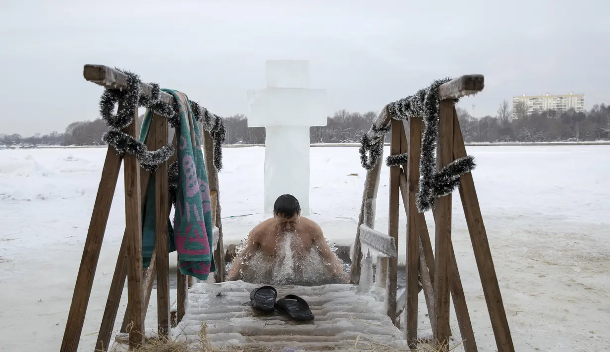 Seorang pria mandi di air dingin sungai Klyazma selama perayaan Epiphany tradisional saat suhu turun hingga sekitar -20 derajat di luar Moskow, Rusia (19/1/2021). berendam di kolam air es diyakini memiliki kekuatan khusus untuk melindungi dan menyembuhkan. (AP Photo/Alexander Zemlianichenko Jr)