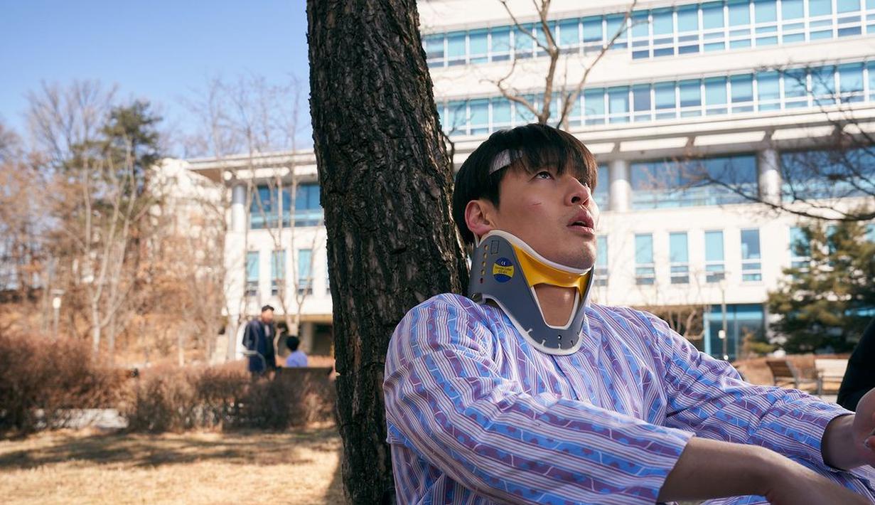 Jung Yeol tampak termenung di bawah pohon dengan baju pasien. Terlihat juga sejumlah luka di tubuhnya. (Foto: Mindmark via Soompi)