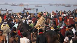 Seorang polisi, maskernya tergantung di dagu, berpatroli saat umat Hindu memadati pertemuan sungai Gangga dan Yamuna untuk ritual mandi pada festival Makar Sankranti di Prayagraj, India, 14 Januari 2022. Di India, orang yang tertangkap tanpa memakai masker akan didenda. (AP Photo/Rajesh Kumar Singh)