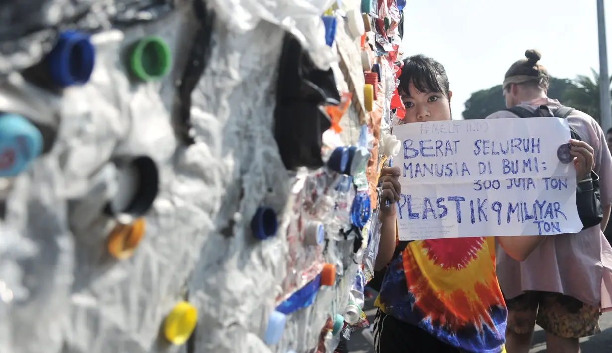 Peserta mengangkat poster dekat instalasi "monster plastik" dalam pawai bebas plastik di Taman Aspirasi Monas, Jakarta, Minggu (21/7/2019). Monster plastik berupa rangka berbentuk menyerupai ikan Angler Fish setinggi 4 meter tersebut dibuat dari 500 kg sampah plastik. (merdeka.com/Iqbal S Nugroho)