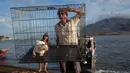 Seorang sukarelawan membawa seekor kucing di dalam kandang saat mereka membawa kembali hewan-hewan dari daerah yang ditinggalkan di kaki gunung berapi Gunung Ruang (latar belakang) di Pulau Tagulandang, Sitaro, Sulawesi Utara, pada 4 Mei 2024. (Ronny Adolof BUOL/AFP)