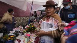 Seorang perempuan membawa barang-barang mini dan uang palsu yang dibeli selama Alasitas Fair tahunan di La Paz, Bolivia pada 24 Januari 2022. Orang-orang membeli replika kecil dari barang-barang yang ingin mereka peroleh sepanjang tahun, seperti rumah, mobil, dan kekayaan. (AP Photo/Juan Karita)