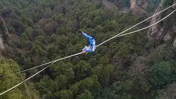 Kontestan berpakaian karakter Avatar bergaya saat melintasi slackline di Pegunungan Huangshizhai di Zhangjiajie, Hunan, China, Minggu (23/12). Pemandangan tersebut memberi sensasi bukit-bukit yang melayang, persis di film Avatar. (STR/AFP)