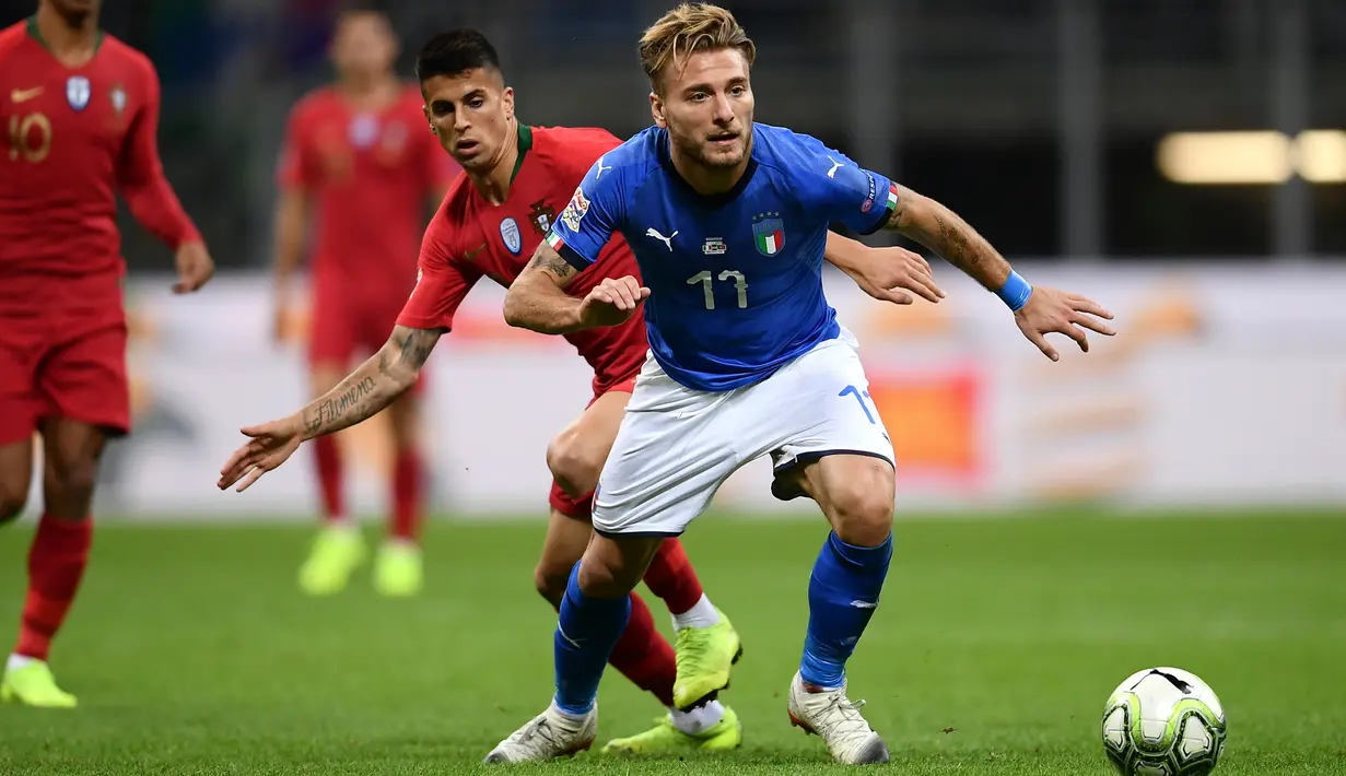 Striker Italia, Ciro Immobile membawa bola dari kawalan bek Portugal, Joao Cancelo selama pertandingan UEFA Nations League di Stadion San Siro di Milan (17/11). Italia bermain imbang 0-0 atas Portugal. (AFP Photo/Marco Bertorello)