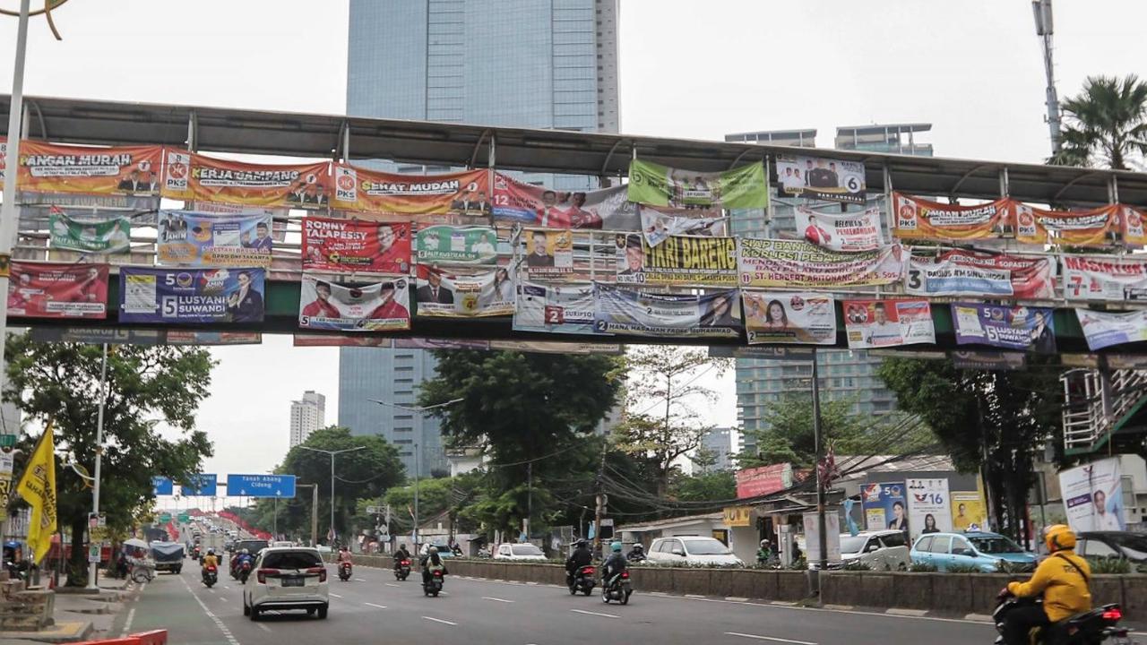 Kendaraan melintas di bawah Jembatan Penyeberangan Orang (JPO) yang tertutup oleh deretan alat peraga kampanye (APK) Pemilu 2024 di Jakarta, Rabu (27/12/2023).<br>
