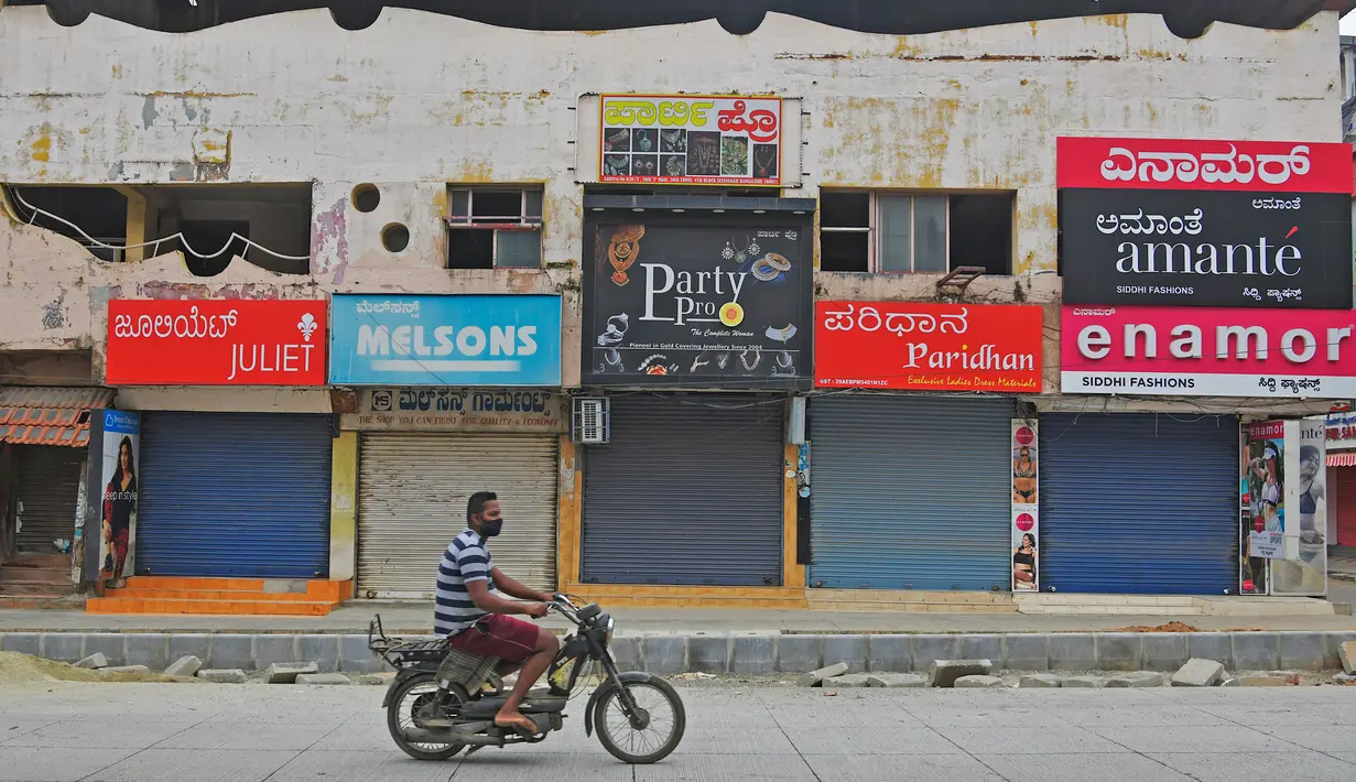 Pengendara motor melintas di depan pertokoan yang tutup di area komersial saat lockdown di Bangalore, Rabu (15/7/2020). Pusat IT India, Bangalore, kembali memberlakukan lockdown selama seminggu dimulai dari 14 Juli 2020 untuk menahan lonjakan kasus Covid-19 yang meningkat. (Manjunath Kiran/AFP)