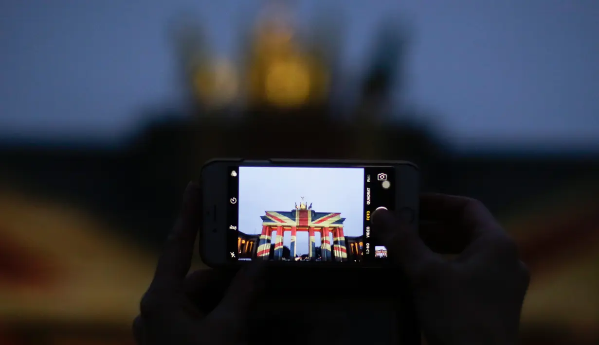 Seorang pengunjung mengambil gambar dari gerbang Brandenburg yang diterangi dengan warna bendera kebangsaan Inggris sebagai bentuk turut berduka cita atas teror London, di ibu kota Jerman, Berlin, Kamis (23/3). (AP Photo/Markus Schreiber)