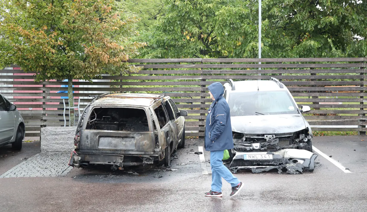 Pejalan kaki melintasi mobil yang hangus terbakar oleh orang tak dikenal di kota Gothenburg, Swedia, Selasa (14/8). Aksi vandalisme besar-besaran ini juga terjadi menjelang pemilu yang digelar pada 9 September ini. (Henrik BRUNNSGARD/TT News Agency/AFP)