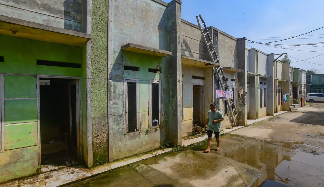 Warga berjalan melewati rumah yang ditinggal pergi pemiliknya akibat kerapkali banjir karena luapan Pesanggrahan yang alirannya menyempit karena longsoran sampah dari Tempat Pembuangan Akhir (TPA) Cipayung di Perumahan Griya Alif, Sawangan, Depok, Jawa Barat, Kamis (14/5/2026). (merdeka.com/Arie Basuki)