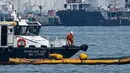 Seorang pekerja pembersihan di atas kapal berdiri di atas alat penyedot minyak selama operasi untuk membersihkan minyak dari tumpahan minyak di dekat terminal pelabuhan Pasir Panjang di Singapura pada tanggal 18 Juni 2024. (ROSLAN RAHMAN/AFP)