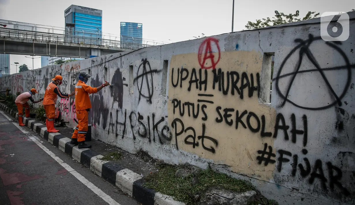 Petugas PPSU membersihkan coretan yang mengotori pembatas jalan pascaunjuk rasa di kawasan DPR/MPR, Jakarta, Jumat (17/7/2020). Coretan tersebut dilakukan oleh massa yang menolak RUU Omnibus Law Cipta Lapangan Kerja di depan Gedung DPR pada Kamis (16/7) kemarin. (Liputan6.com/Faizal Fanani)