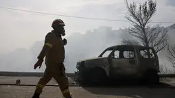 Seorang petugas pemadam kebakaran berjalan di samping mobil yang terbakar selama kebakaran hutan di pinggiran Voula, di selatan Athena, Yunani, Sabtu, 4 Juni 2022. Awan asap tebal imbas dari kebakaran hutan itu pun menganggu aktivitas di wilayah pinggiran selatan Yunani. (AP Photo/Yorgos Karahalis)