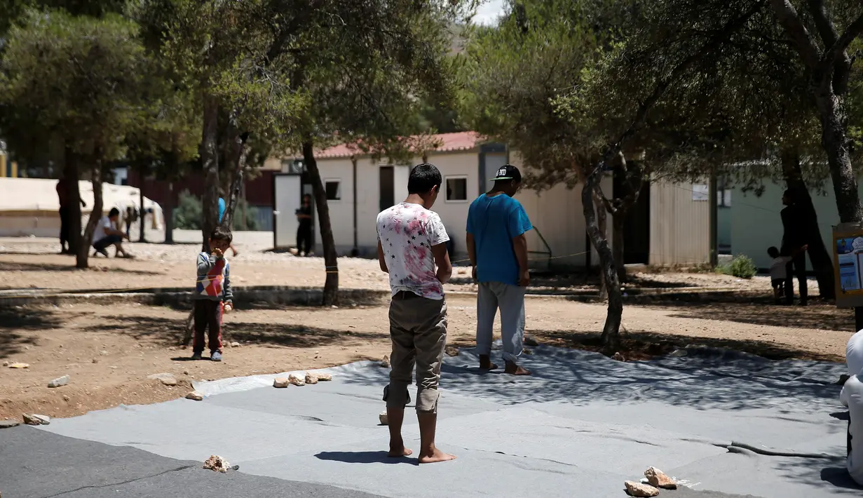 Seorang anak mengamati imigran yang sedang melaksanakan salat pada hari pertama Ramadan, di kamp pengungsian milik pemerintah Yunani di Schisto, Athena, Senin (6/6). Imigran membuat masjid darurat di sebuah halaman terbuka. (REUTERS/Alkis Konstantinidis)