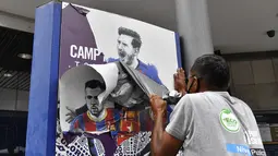 Seorang pekerja melepas poster-poster yang menampilkan pemain depan Barcelona Lionel Messi di stadion Camp Nou di Barcelona (10/8/2021). Prancis menunggu dengan tidak sabar Lionel Messi dengan para pendukung berkumpul di luar lapangan Paris Saint-Germain. (AFP/ Pau Barrena)