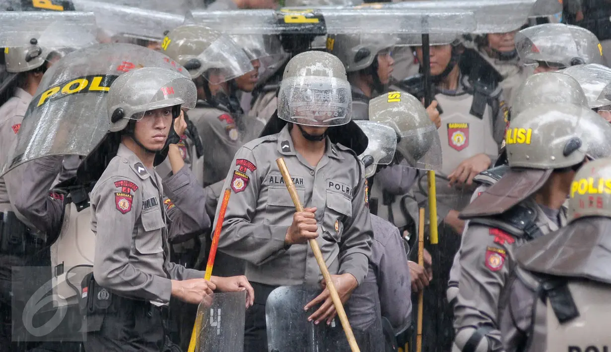 Petugas kepolisian menggunakan tameng untuk berteduh dari hujan saat menjaga aksi Hari Buruh di Jalan Medan Merdeka, Jakarta, Senin (1/5). (Liputan6.com/ Yoppy Renato)