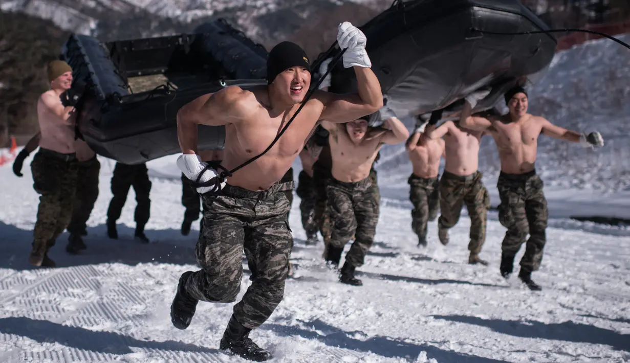 Gabungan tentara Korea Selatan dan AS mengangkat perahu karet saat latihan musim dingin di Pyeongchang, Korea Selatan (24/1). Mereka latihan dengan setengah telanjang untuk mengetes ketahanan fisik. (AFP/Ed Jones)