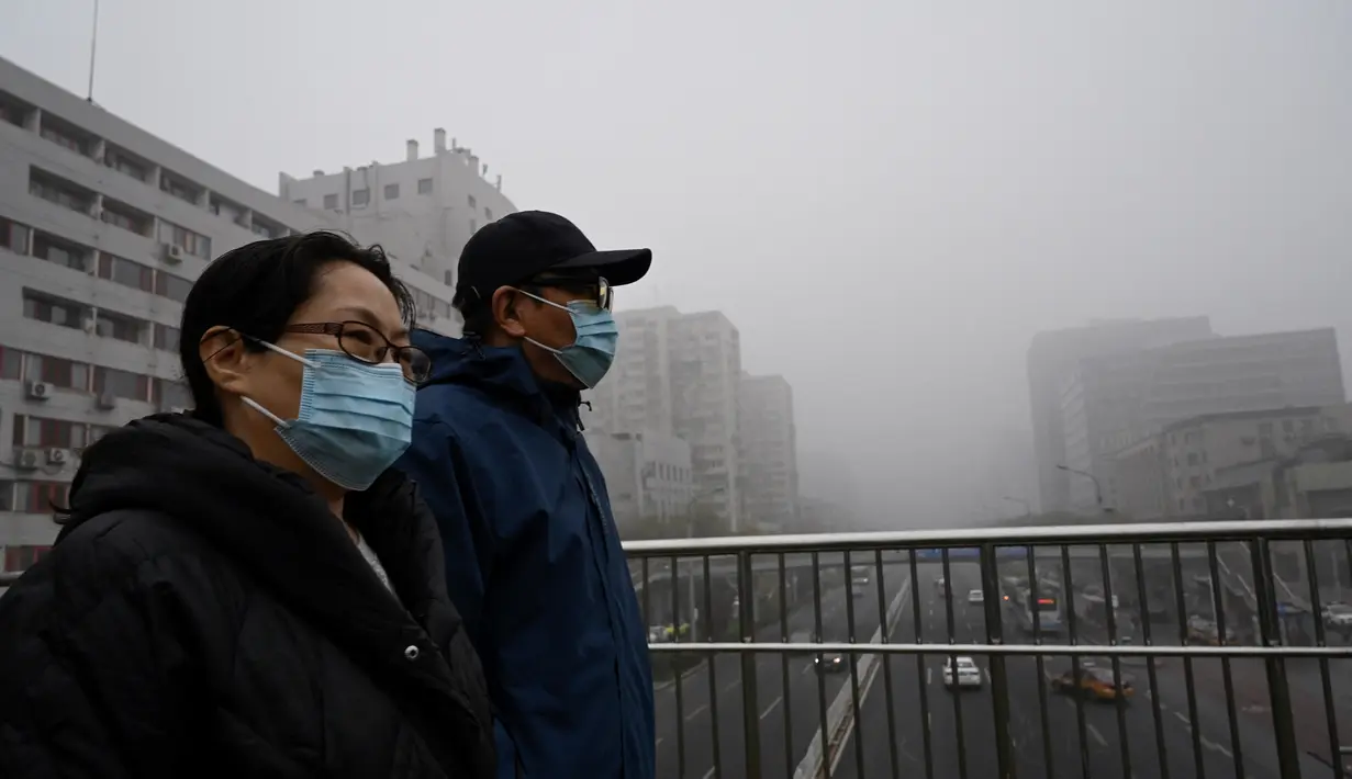 Orang-orang yang memakai masker melintasi jalan layang pada hari yang berkabut dan tercemar di Beijing, Sabtu (6/11/2021). Jalan raya dan taman bermain sekolah di Beijing ditutup pada Jumat (5/11) karena polusi kabut asap yang tebal, setelah China meningkatkan produksi batu bara. (JADE GAO/AFP)