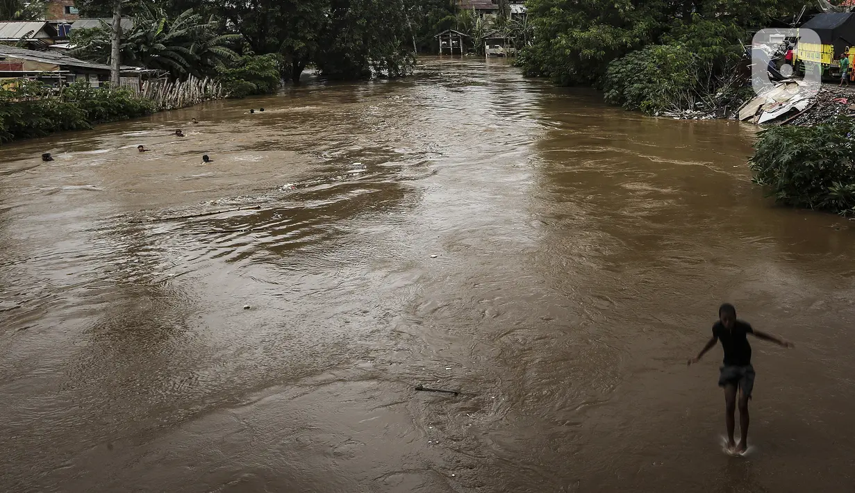 Seorang anak melompat ke Sungai Ciliwung saat banjir melanda Jalan Bina Warga Rt 005/Rw 07 Kelurahan Rawa Jati, Jakarta, Senin (8/2/2021). Banjir setinggi 60-190 cm tersebut disebabkan oleh luapan air Sungai Ciliwung dan curah hujan Jakarta yang tinggi. (Liputan6.com/Johan Tallo)